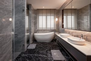 White light is strategically placed away from the mirror to prevent shadows during makeup, or precise work like tweezing or shaving and the optimized lighting coverage is just right to illuminate the entire space. ​A pendant light is added to brighten the intimate tub area while setting the mood just right for a relaxing evening. Just like the master bathroom, this common bath displays exquisite touches of natural stone with a striking speckled stone finish for the walls. ​A floating vanity with handleless drawers gives a clean and modern look to the cozy bathroom.